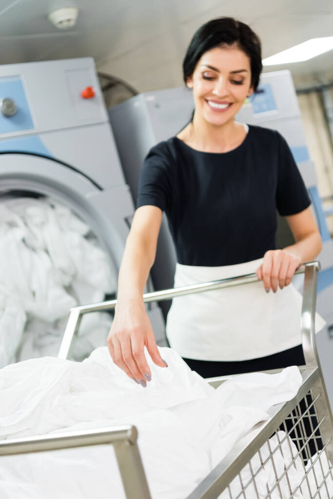 Tidy Loads Laundry employee grabbing folded sheets from basket providing commercial laundry service in Jacksonville, Nocatee, St. Johns