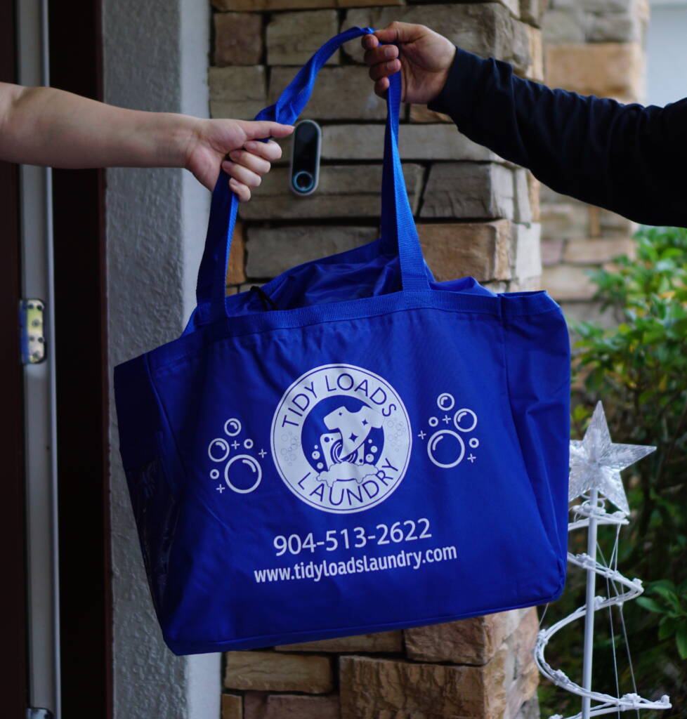 An employee from Tidy Loads Laundry giving a customer a personalized reusable bag at their door with the Tidy Loads Laundry logo