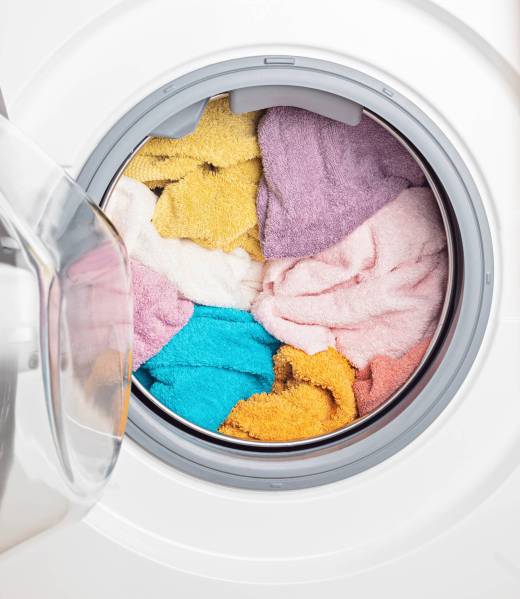 Washing machine that is open with colorful towels inside of it referring to Tidy Loads Laundry's wash and fold laundry services in Jacksonville, Nocatee, St. Johns and beyond